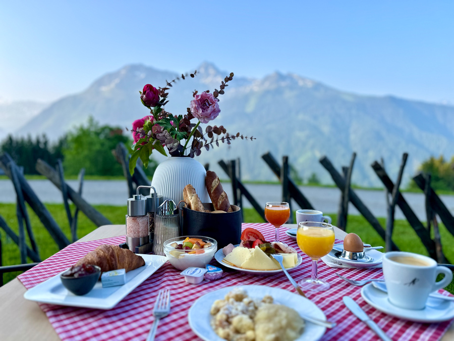 Fein gedeckter Frühstückstisch mit original Montafoner Brösel und regionalen Spezialitäten vor einem traumhaften Panoramablick auf die Berge des Verwallgebirges in den österreichischen Alpen.